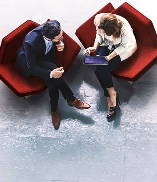 Two people sitting on red chairs looking at a device